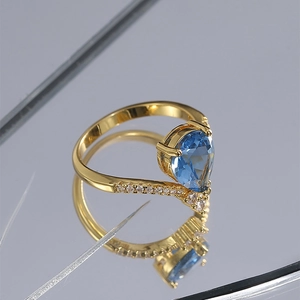 Vintage gold ring with pear-cut blue zircon and small clear side stones on a mirror surface