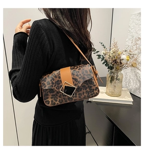 Leopard print shoulder bag with brown leather strap worn by model in a stylish room