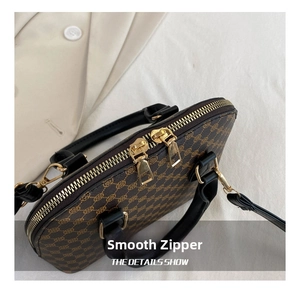 Detail view of smooth golden zippers and retro monogram texture on dark brown shell bag