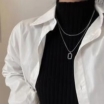 Detail of a silver double-layered necklace with a geometric rectangular pendant on a model