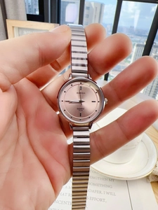 Detailed shot of a silver chain watch with a rose gold dial held by a hand in soft light