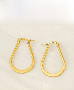 Detailed view of gold U-shaped stainless steel earrings on a beige textured fabric