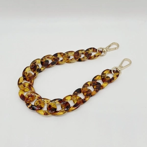 Detail of tortoiseshell acrylic chain strap with light gold metal lobster clasps on white background