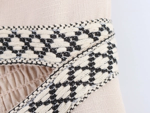 Dettaglio del tessuto di lino beige con spalline intrecciate a motivi geometrici neri