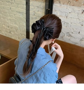 Detail of a large black satin bow scrunchie styled on long hair in a ballet core aesthetic