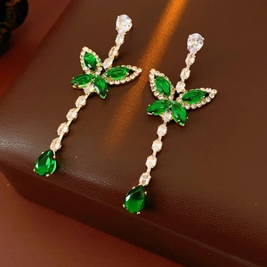 Detail of butterfly drop earrings with green and white crystals on golden metal base