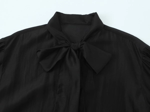 Close-up of the elegant bow-tie neckline on a smooth black satin blouse for women