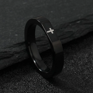 Close-up of a faceted black stainless steel ring with a silver cross on textured stone