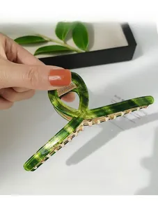 Detailed close-up of green marble acetate hair claw clip with golden metal teeth