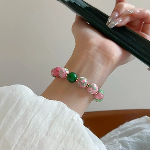 Detailed shot of gold-plated bracelet with pink floral beads and a green glass bead