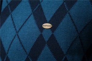 Macro view of blue diamond pattern knitwear with bronze metal brand tag detail