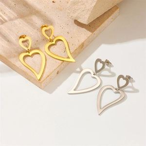 Minimalist gold and silver hollow heart earrings on beige stone base background