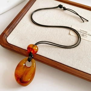 Macro detail of amber resin teardrop pendant with swirl pattern on wax cord