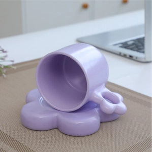 Detail of purple ceramic mug with chubby handle on a flower shaped saucer
