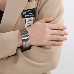 Macro view of stacked silver polished steel bangles worn with a beige blazer sleeve