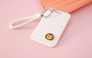 Close-up of white plastic card holder with lion charm, woven wristlet and metal keyring