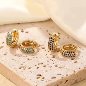Élégantes créoles dorées avec zircons turquoise et noirs sur un tissu de soie