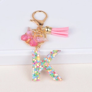 Close-up of letter K keychain with resin colorful sequins and pink butterfly tassel