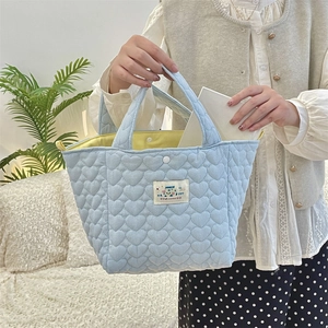 Close-up of blue quilted heart handbag with white snap button and yellow inner lining