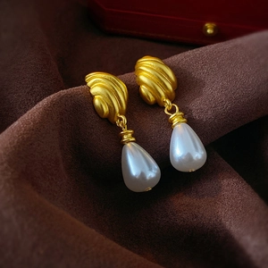 Close-up of vintage gold metal earrings with white teardrop pearls on velvet