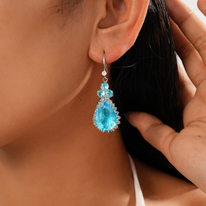 Close-up of elegant blue teardrop gemstone earrings with zircon floral accents on model