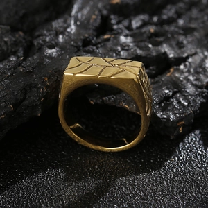 Close-up of golden stainless steel signet ring with geometric textured top on dark background