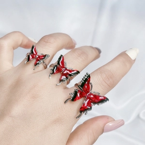 Detail of red and black enamel butterfly rings on white silk background with model hand