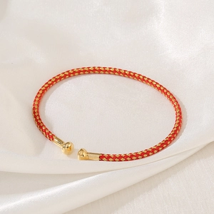 Detail of red and gold woven bracelet featuring polished spherical metal end caps