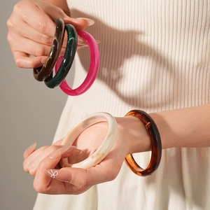 Close-up of five colorful resin bangles in acetate texture worn by a model in soft light