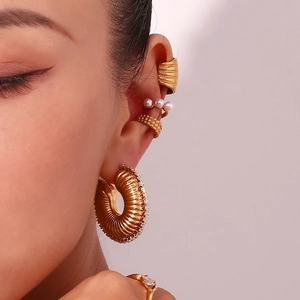 Detail of 18K gold irregular hoop earring and pearl ear cuff set worn on a model