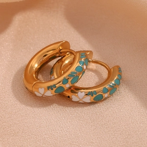 Macro view of gold hoop earrings featuring detailed blue and white enamel floral patterns