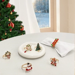 Golden metal Christmas napkin rings with reindeer, tree and wreath designs on white napkins