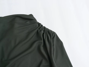 Detailed view of the elegant ruched shoulder and pleated texture on a dark green midi dress