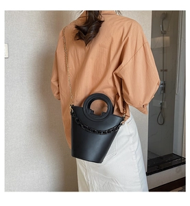Fashionable black bucket bag with circular handle and dual chain straps shown on a model