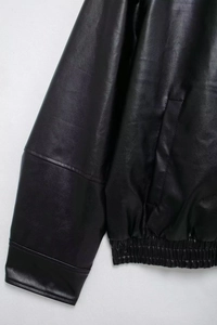 Detail shot of black faux leather bomber jacket showing elastic hem and grainy texture