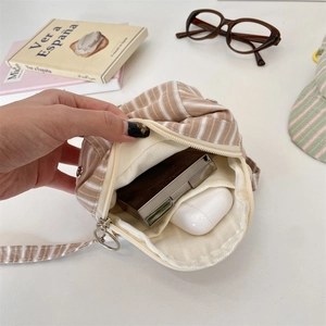 Detail of striped canvas crossbody bag showing internal compartments for makeup items