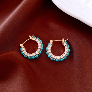 Detail of gold hoop earrings with white zircon and turquoise on dark silk fabric