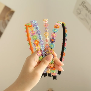 Hand holding assorted colorful embroidered daisy headbands in orange, purple, and beige