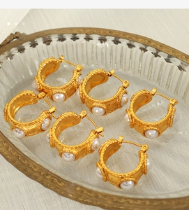 Detailed close-up of 18k gold C-shape earrings with inlaid white pearls on a glass tray