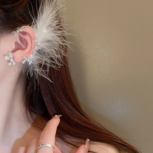 Macro shot of a silver feather ear cuff with rhinestone bows worn on a model