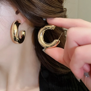 Detailed close-up of chunky golden C-shaped hoop earrings with a polished metallic finish