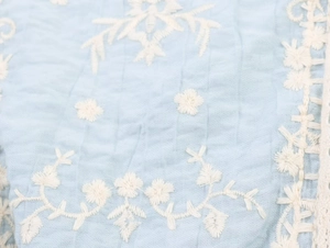 Macro detail of light blue crepe fabric with white floral embroidery for summer tops