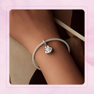 Close-up of a silver mesh bracelet with a heart bow pendant worn on a female wrist