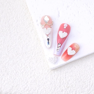 Close-up of pink peach gradient nails with heart pearls, rhinestones and golden chains