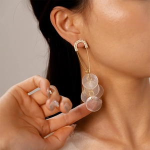 Detail view of gold safety pin earrings with layered shell discs and sparkling zirconias