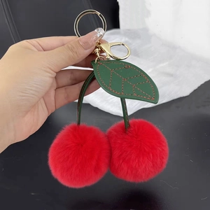 Detail of red faux rabbit fur cherry keychain with green leather leaf held in hand