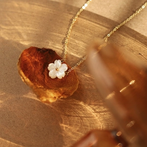 Detail of white shell flower pendant on thin gold chain resting on a dry leaf