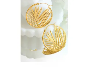 Macro shot of gold bamboo leaf hoop earrings with a mirror reflection on white ceramic