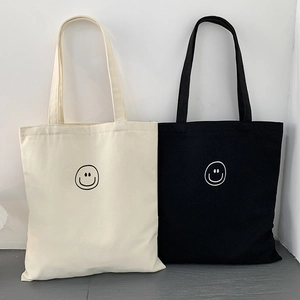 Detail of off-white and black canvas tote bags with minimalist smiley face print