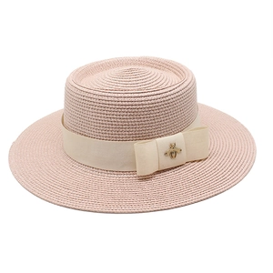 Detail of pink straw boater hat with cream ribbon bow and golden bee accessory